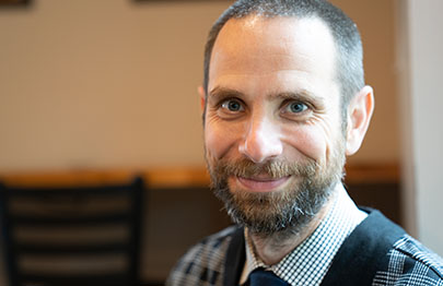 A close up of a middle-aged man, with a beard and dressed in a tie.